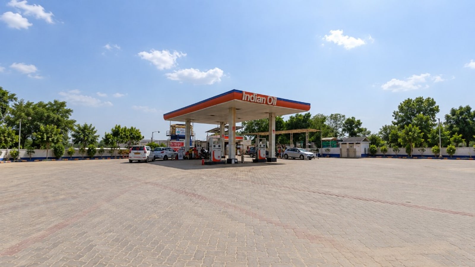 Wide view of a fuel station forecourt with vehicles at the pumps