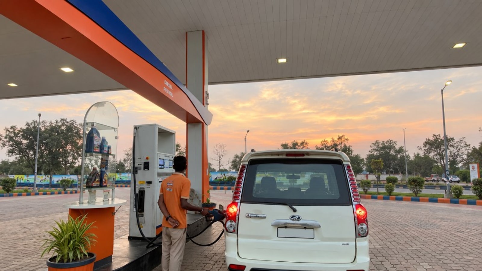 Attendant refueling a vehicle at sunset under the station canopy